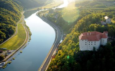 reka Kostanjevica, ki se vije po zeleni pokrajini in grad Rajhenburg slikano iz zraka