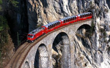 vlak bernina express, redeče barve, vozi po viaduktu v skalah