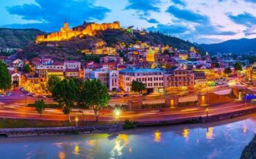 večerna slika mesta Tbilisi, z reko v ospredju in trdnjavo na vrhu griča