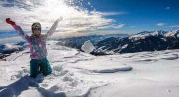 A woman sprinkling powder snow around her on top of Katschberg in Austria. She is happy and joyful. Panoramic view on the surrounding mountains. Winter wonderland, Clear and sunny winter day